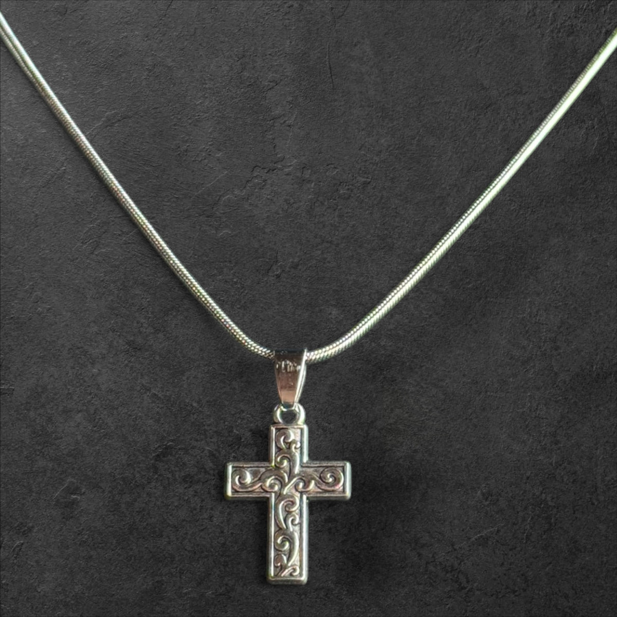 Silver cross pendant necklace featuring intricate filigree scrollwork on a polished snake chain.